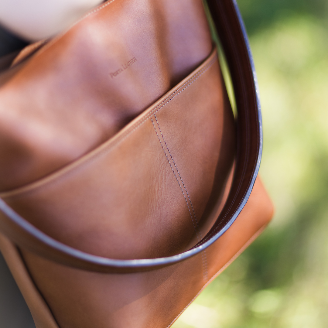 Close-up of a heritage brown leather bag from Porta Leather with visible stitching detail, blurred green background