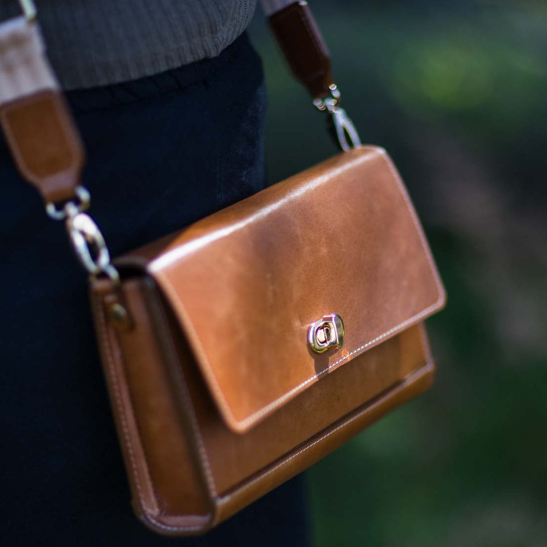 Tan Porta Leather Jenna handbag with a crossbody strap worn by a person against a blurred green background
