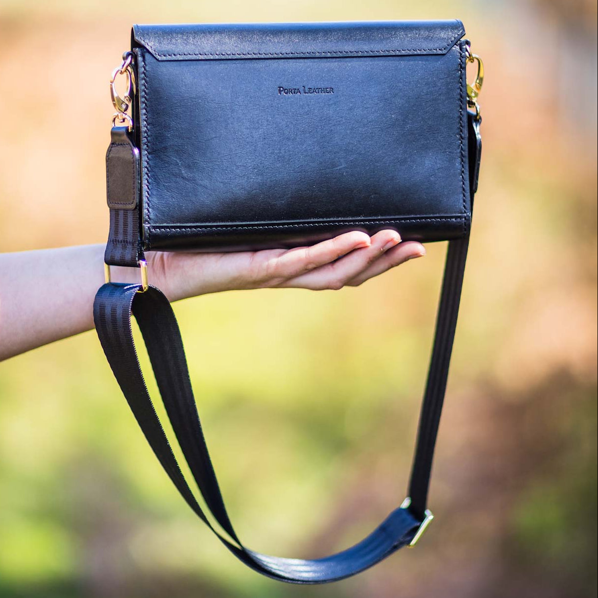 Black Porta Leather handbag with crossbody strap held by a person with a blurred natural background