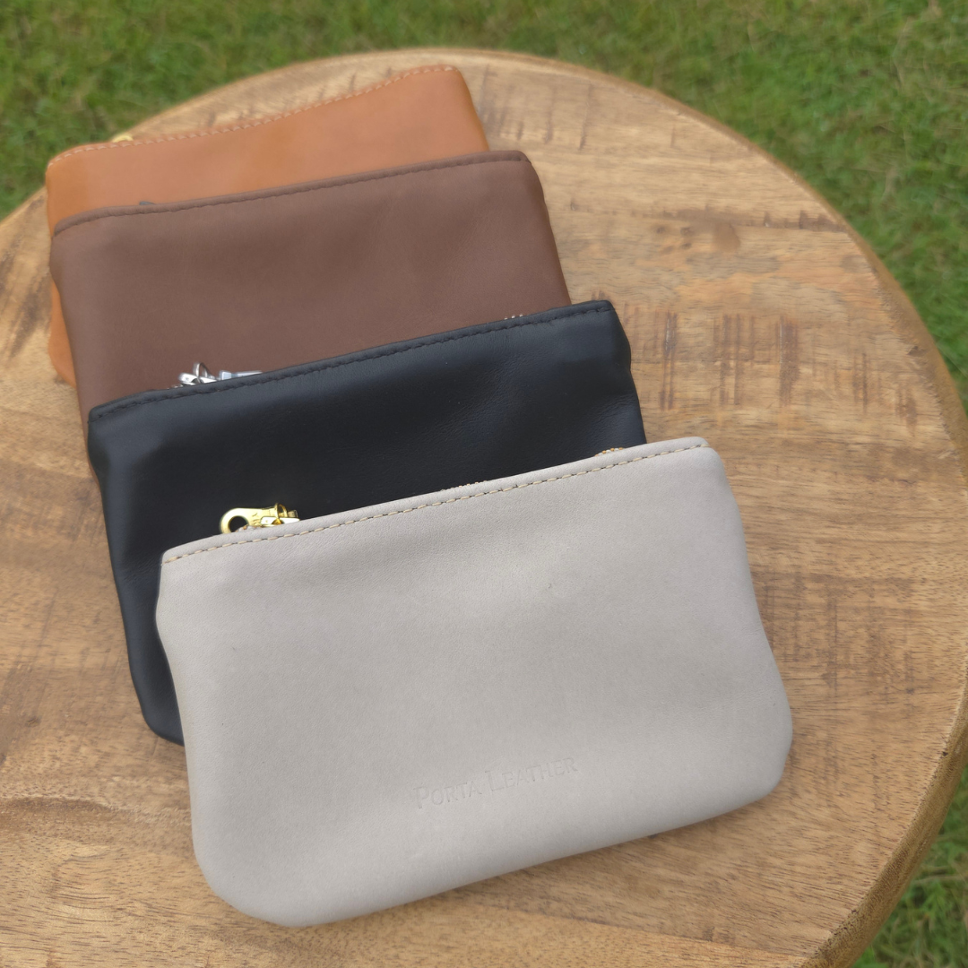 Collection of Porta Leather mini pouches sitting on a stool in brown, black, tan and grey.