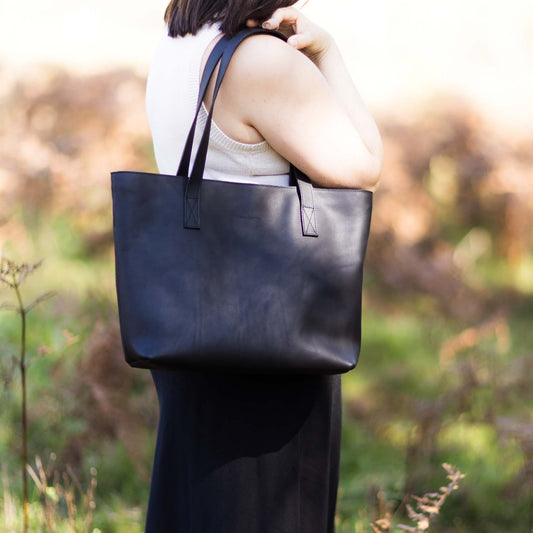 Person holding a black tote bag in a natural setting