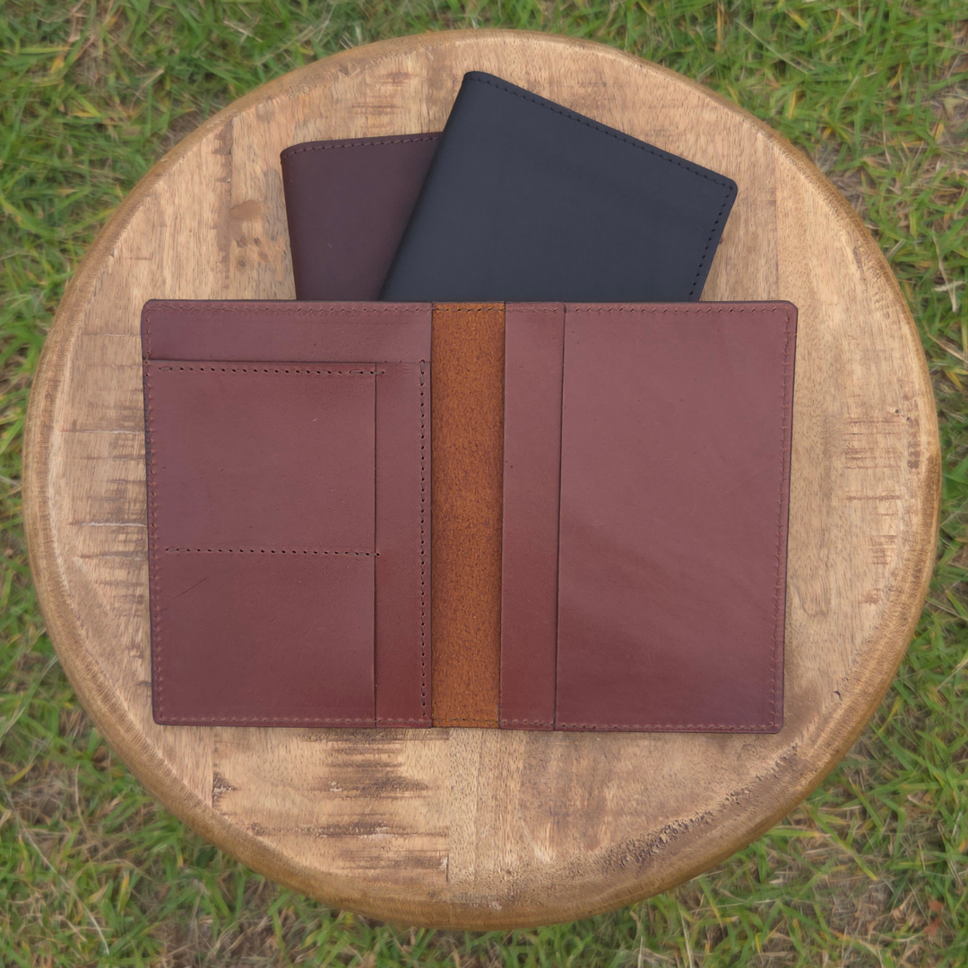 Two Porta Leather passport wallets closed and one showing the open view, on a wooden stool outdoors.
